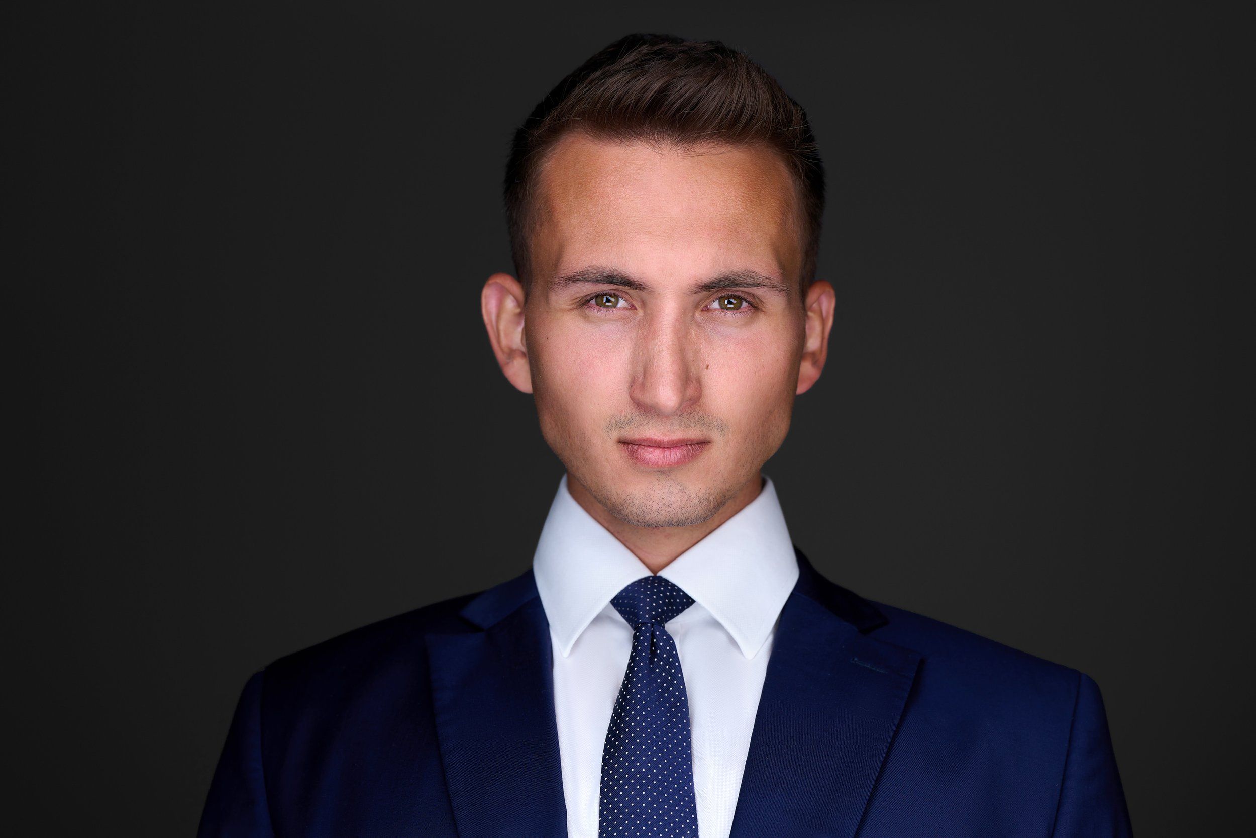 Businessportrait eines jungen Mannes im dunkelblauen Anzug mit Krawatte vor dunklem Hintergrund, fotografiert im Studio in Köln