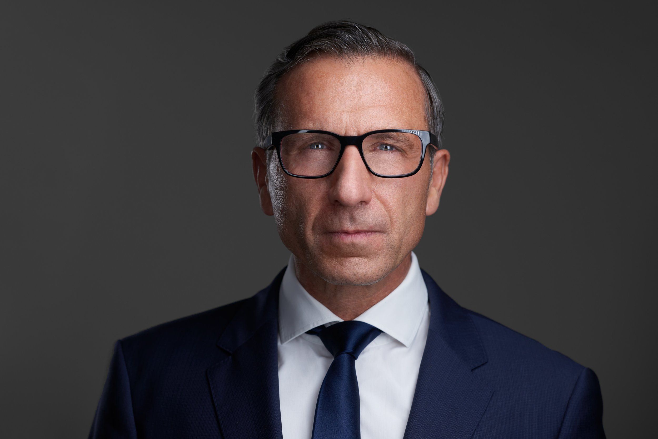Businessportrait eines Managers mit Brille im Anzug mit Krawatte vor grauem Hintergrund, fotografiert im Studio in Köln