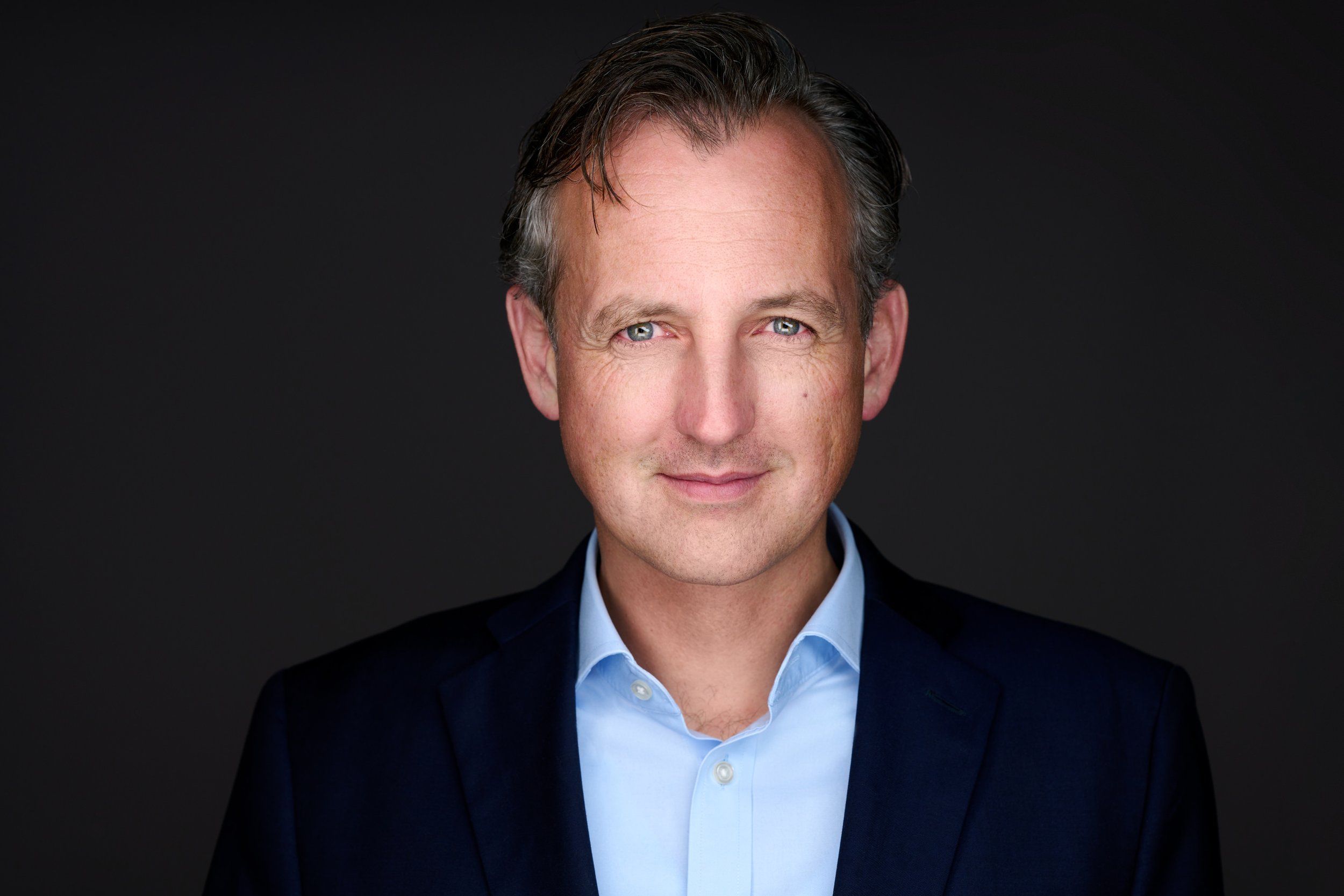 Businessportrait eines Mannes im dunklen Anzug mit hellblauem Hemd vor dunklem Hintergrund, fotografiert im Studio in Köln