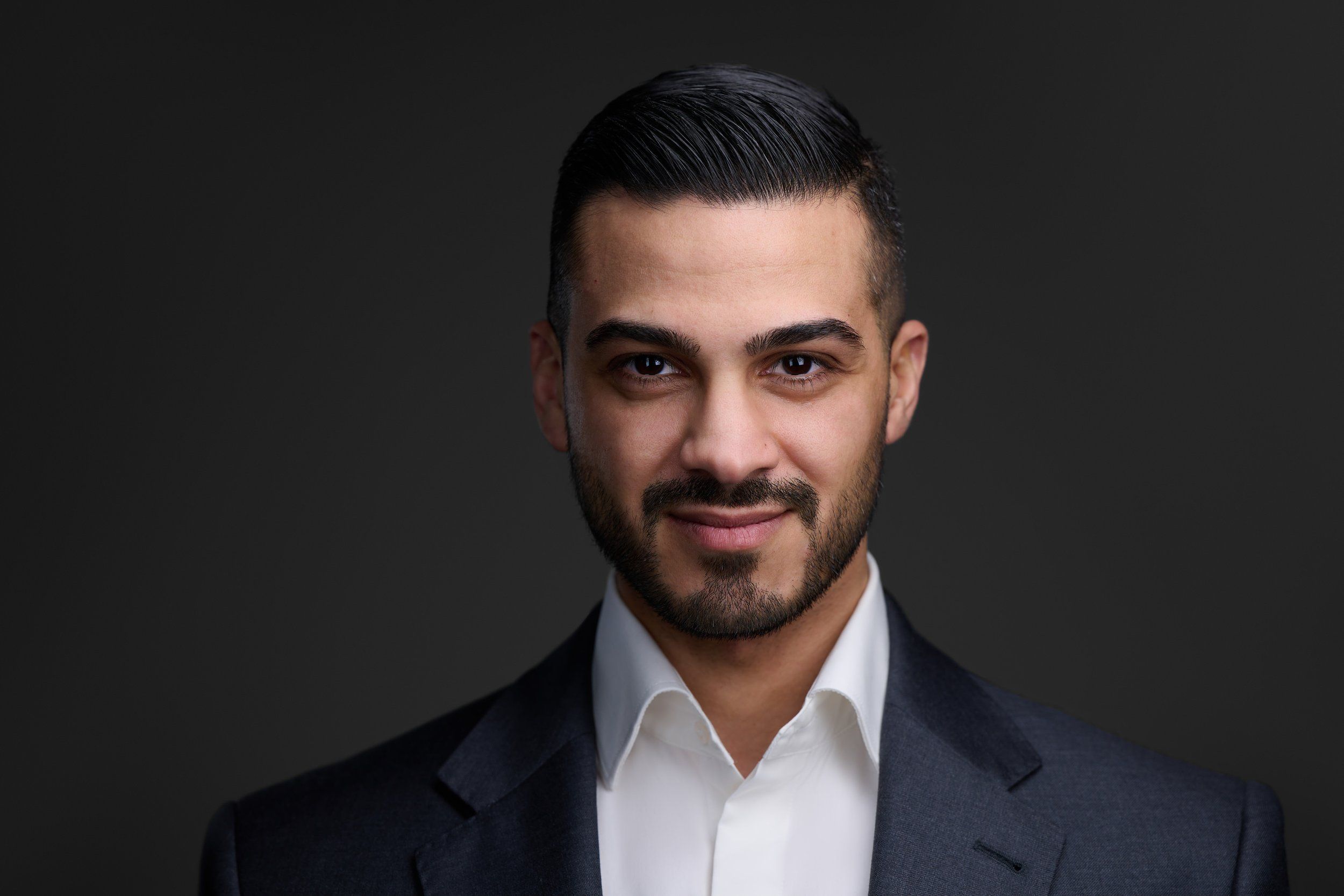 Businessportrait eines Mannes mit dunklem Haar und Bart im grauen Anzug vor dunklem Hintergrund, fotografiert im Studio in Köln