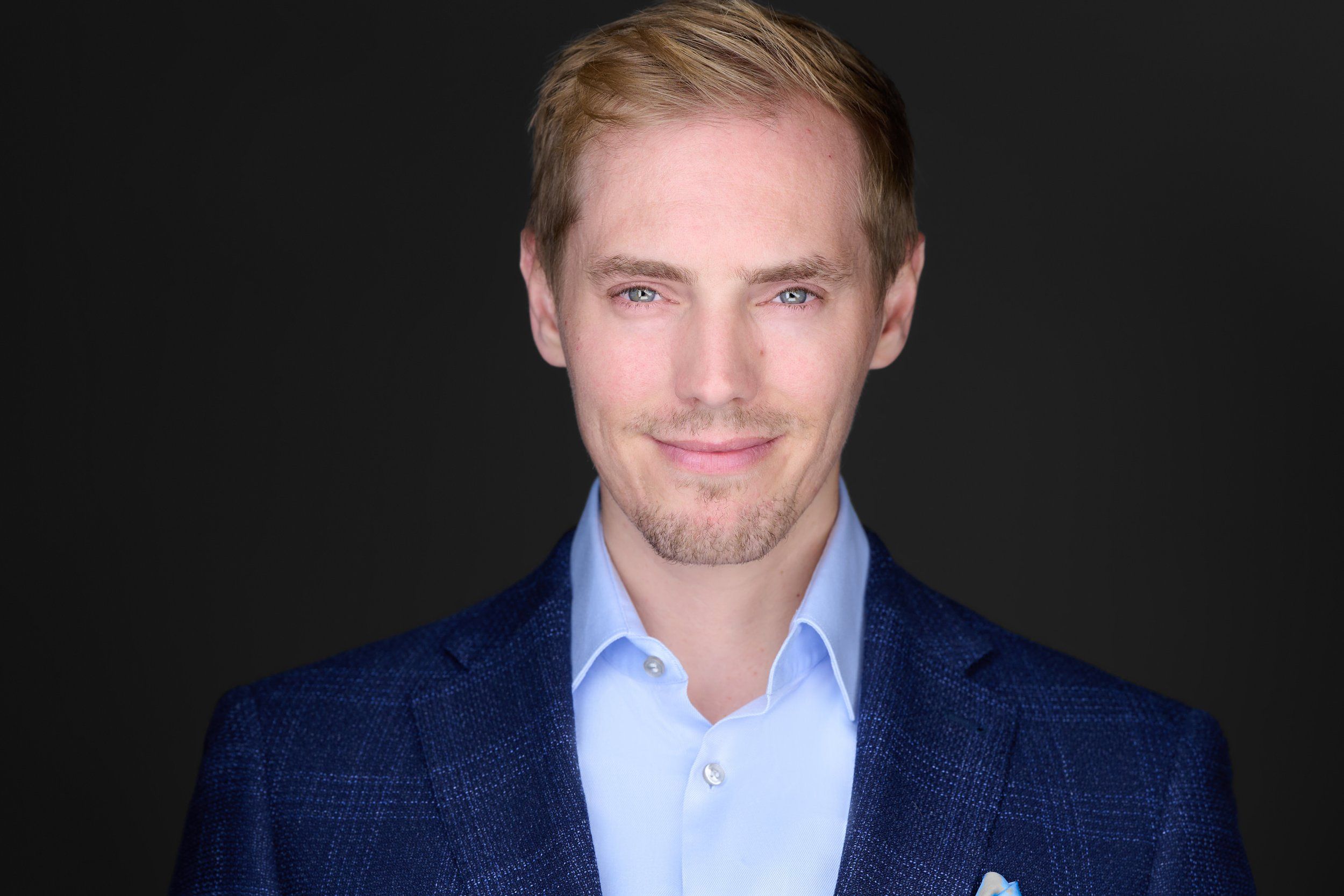 Businessportrait eines blonden Mannes im blauen Karo-Sakko vor dunklem Hintergrund, fotografiert im Studio in Köln