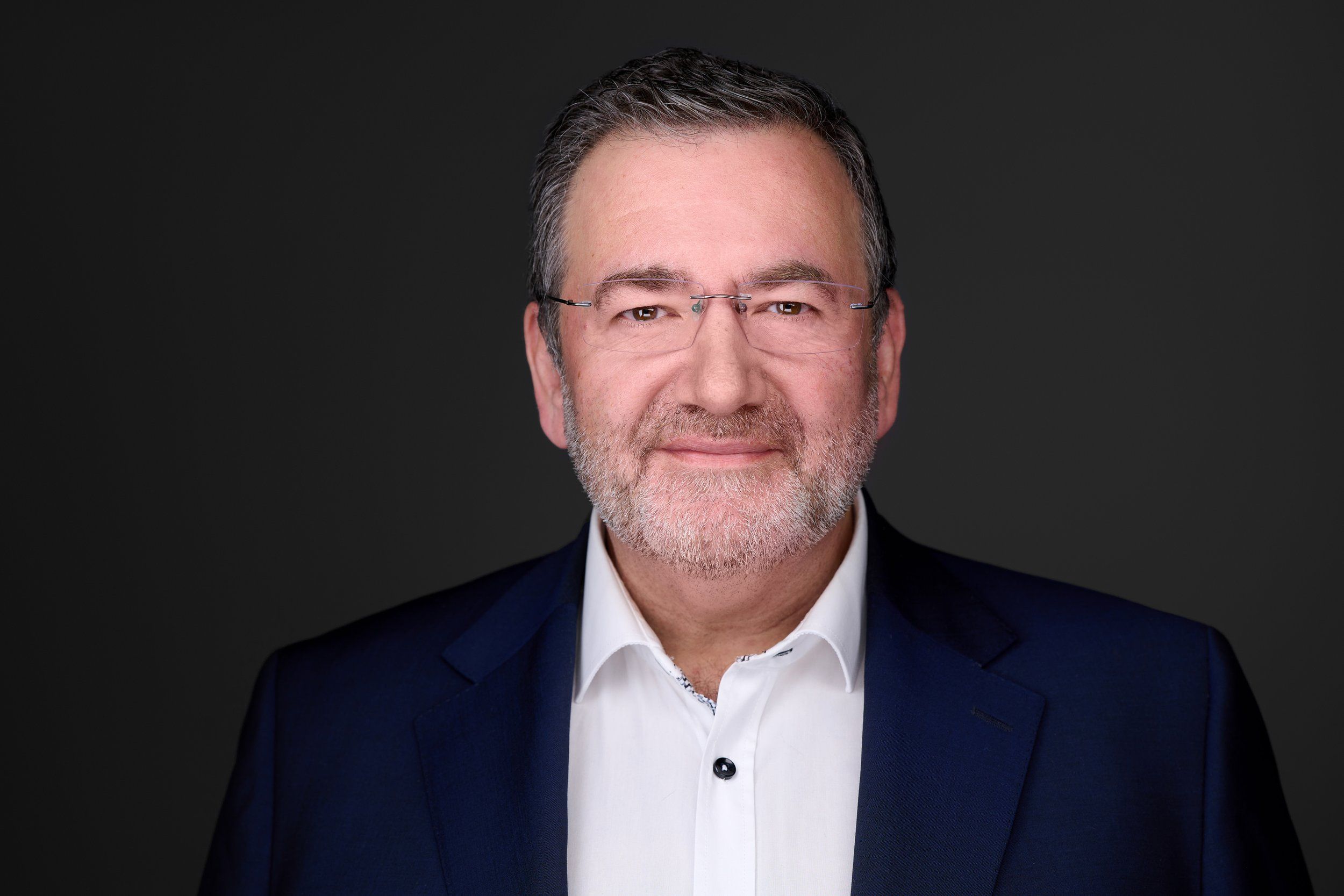 Businessportrait eines Mannes mit Brille und grauem Bart im dunkelblauen Anzug vor dunklem Hintergrund, fotografiert im Studio in Köln