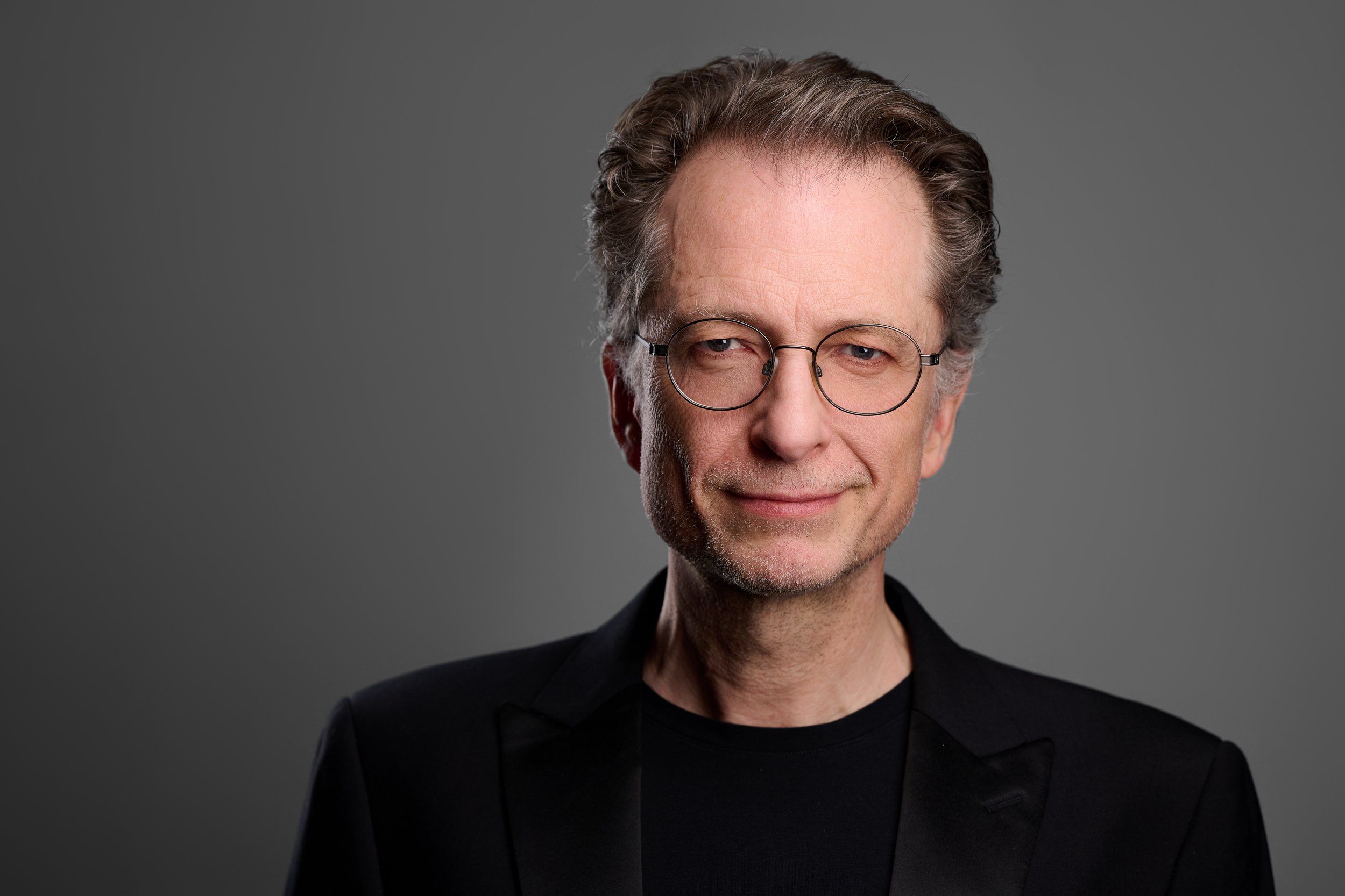 Businessportrait eines Mannes mit Brille im schwarzen Sakko vor grauem Hintergrund, fotografiert im Studio in Köln