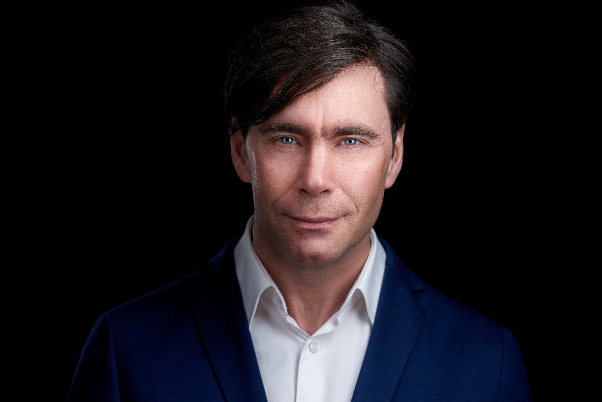 Businessportrait eines Mannes mit dunklem Haar im blauen Sakko vor schwarzem Hintergrund, fotografiert im Studio in Köln