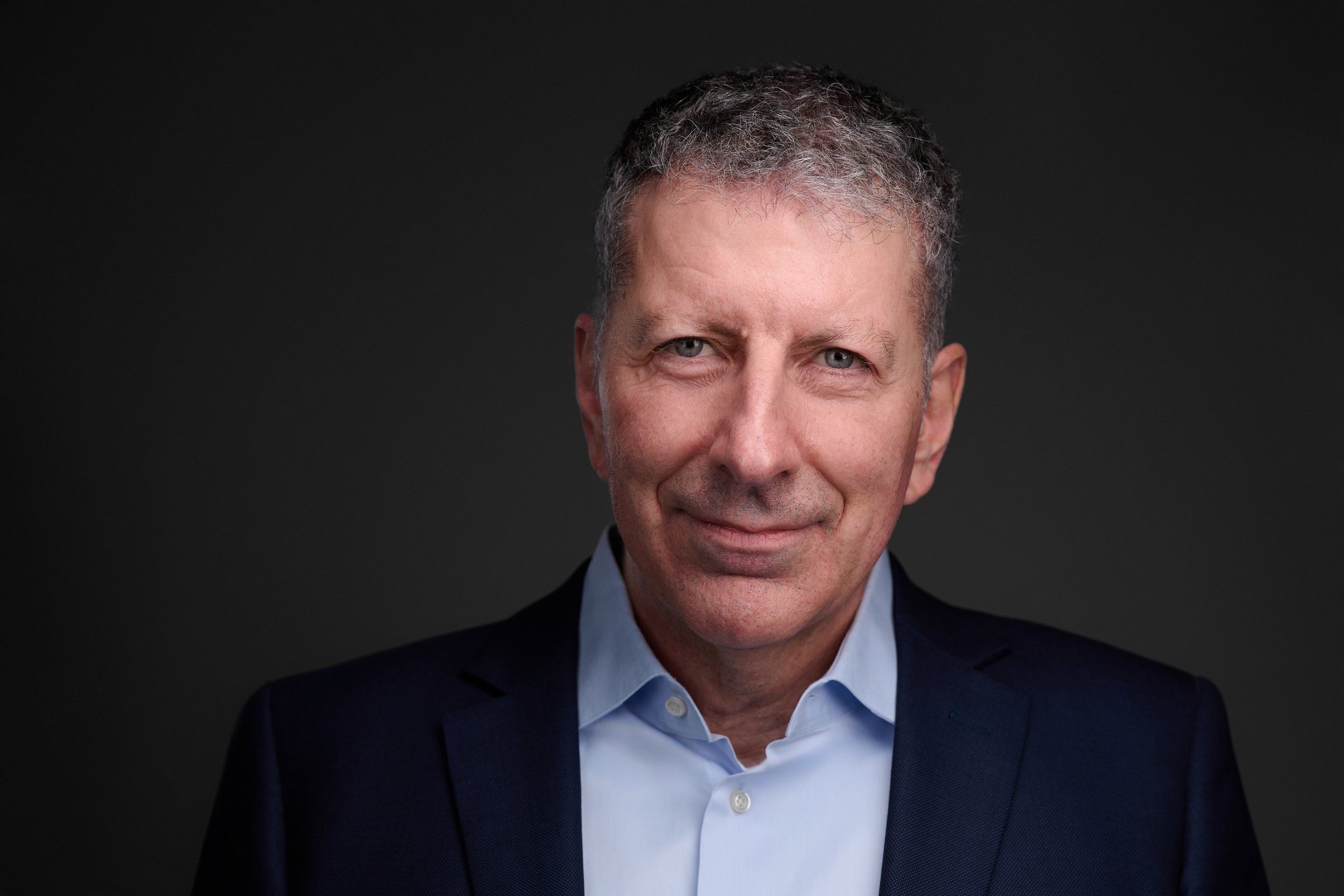 Businessportrait eines Mannes mit grauen Haaren im dunklen Anzug vor dunklem Hintergrund, fotografiert im Studio in Köln