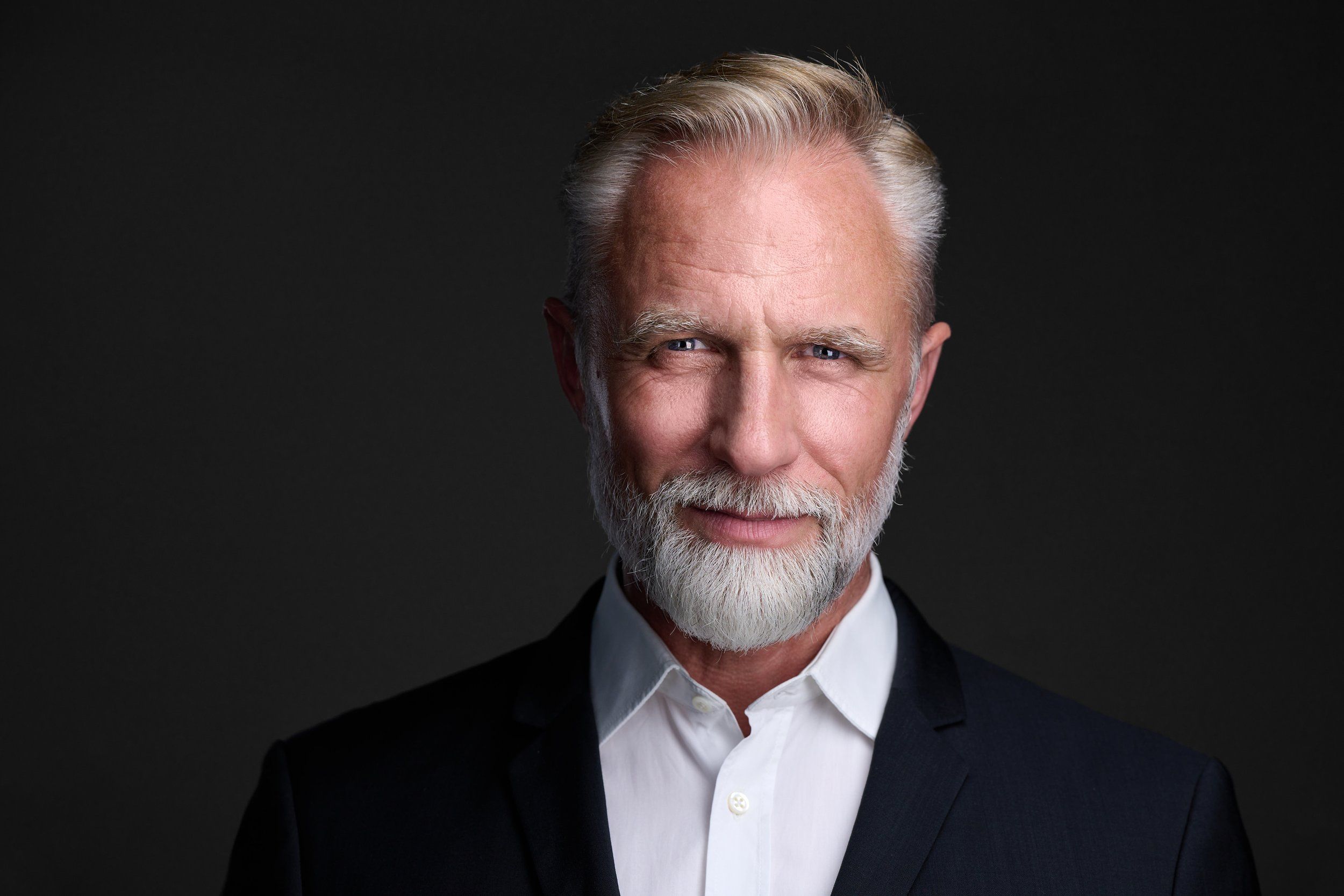 Businessportrait eines Mannes mit grauem Haar und weißem Bart im Sakko vor dunklem Hintergrund, fotografiert im Studio in Köln