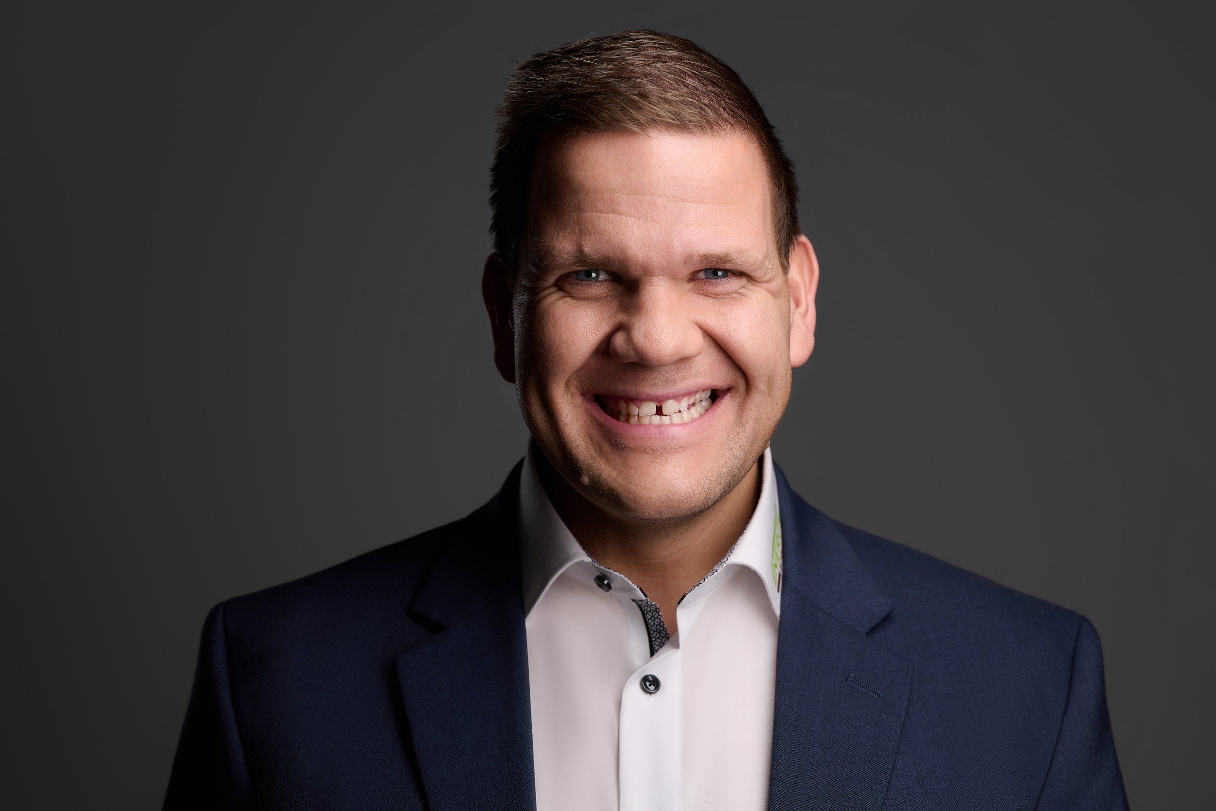 Businessportrait eines lachenden Mannes im dunkelblauen Anzug vor dunklem Hintergrund, fotografiert im Studio in Köln
