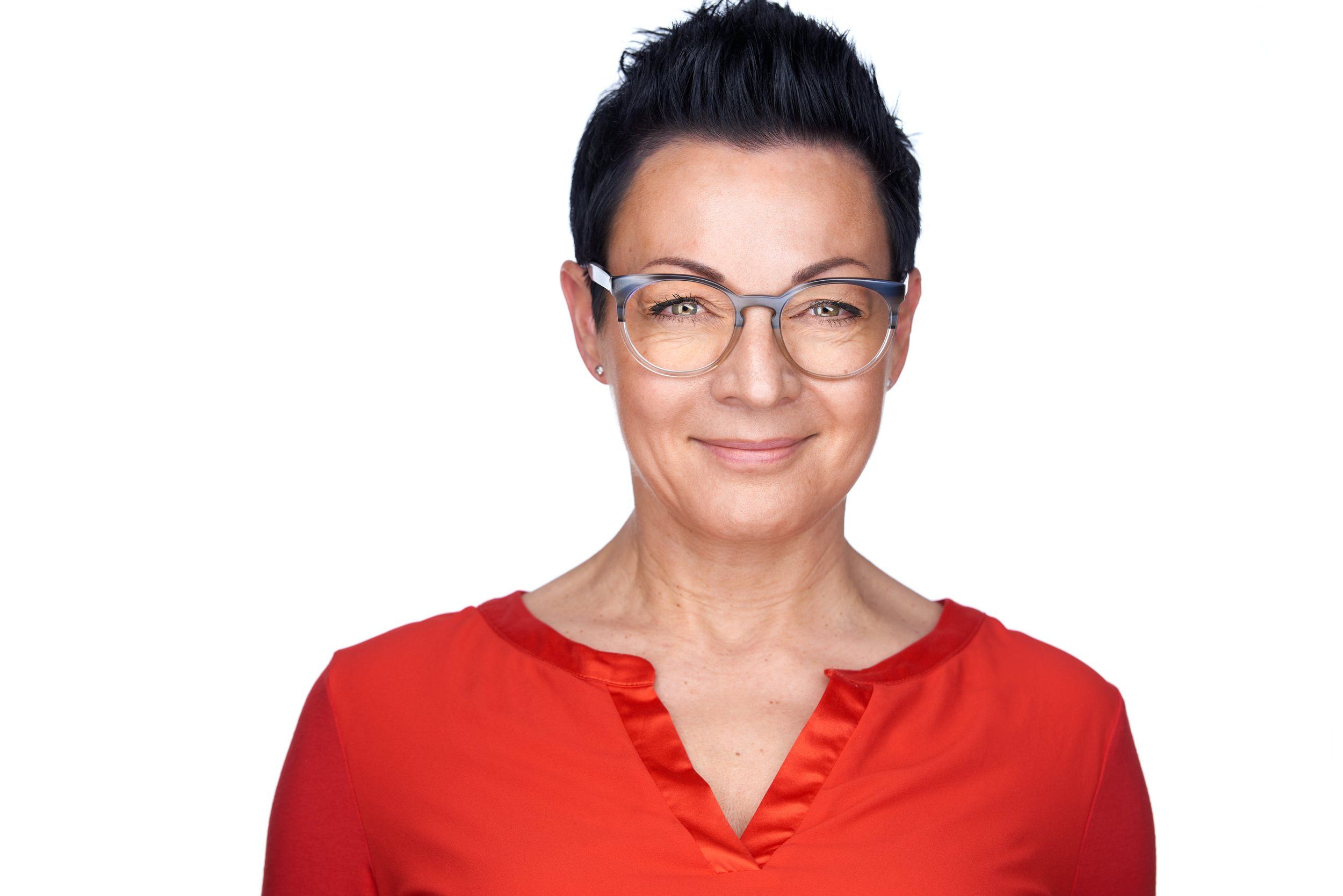 Headshot einer Frau mit kurzen schwarzen Haaren und Brille in roter Bluse vor weißem Hintergrund, fotografiert im Studio in Köln