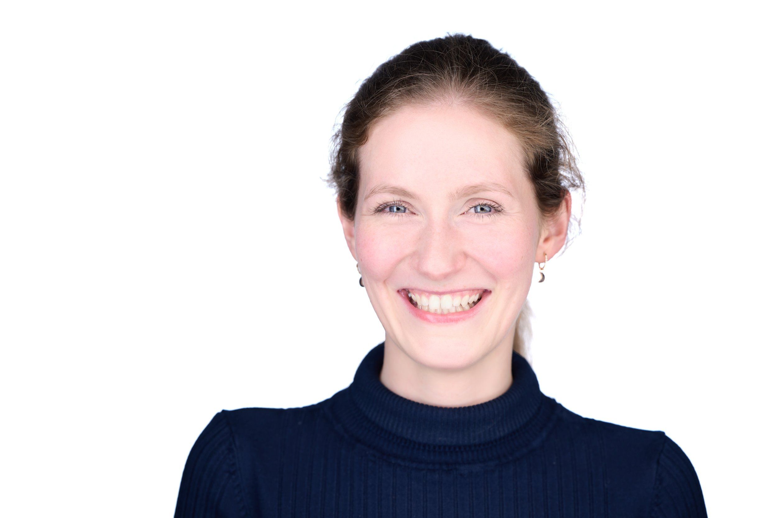 Headshot einer lachenden jungen Frau im dunkelblauen Pullover vor weißem Hintergrund, fotografiert im Studio in Köln