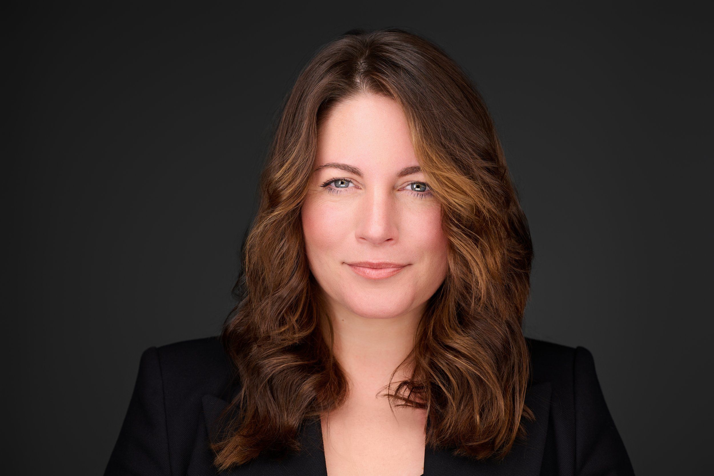 Headshot einer Frau mit langen, gewellten braunen Haaren vor dunklem Hintergrund, fotografiert im Studio in Köln