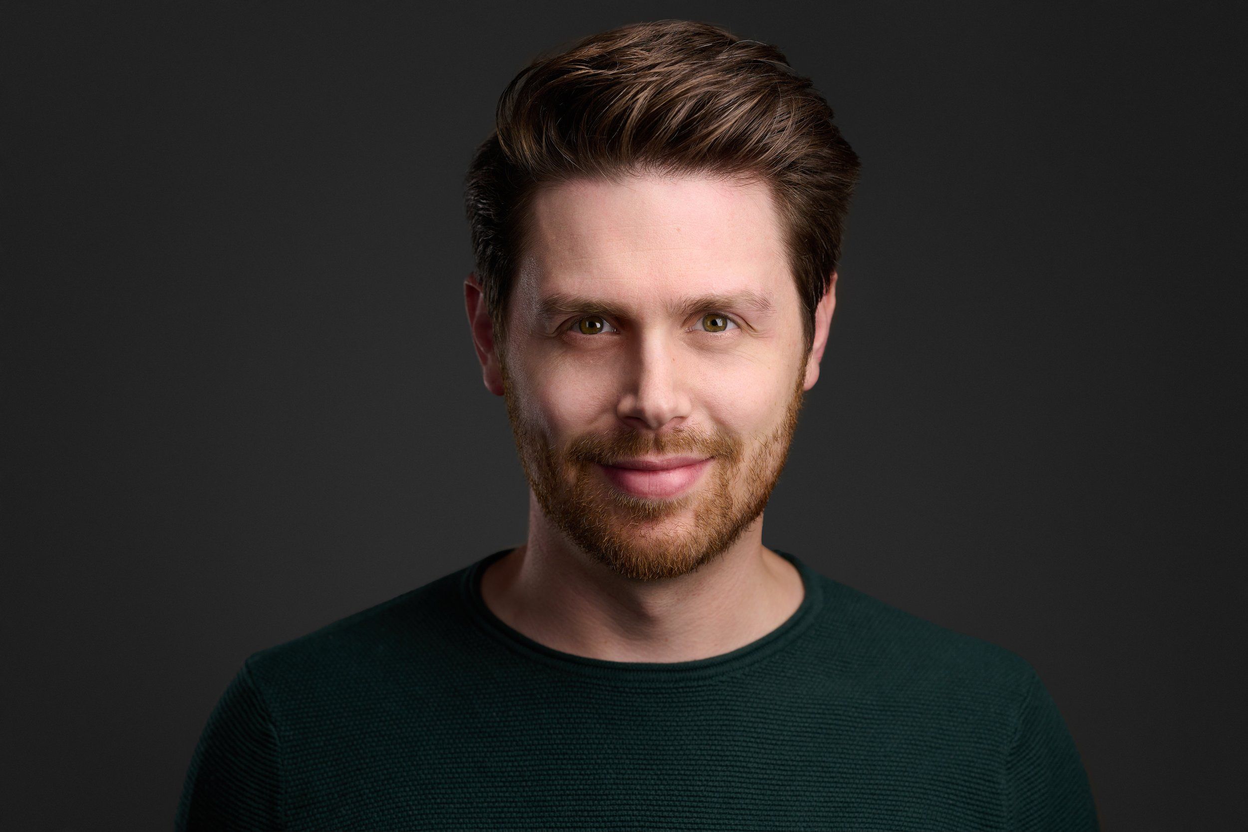 Headshot eines Mannes mit Bart im dunkelgrünen Pullover vor dunklem Hintergrund, fotografiert im Studio in Köln
