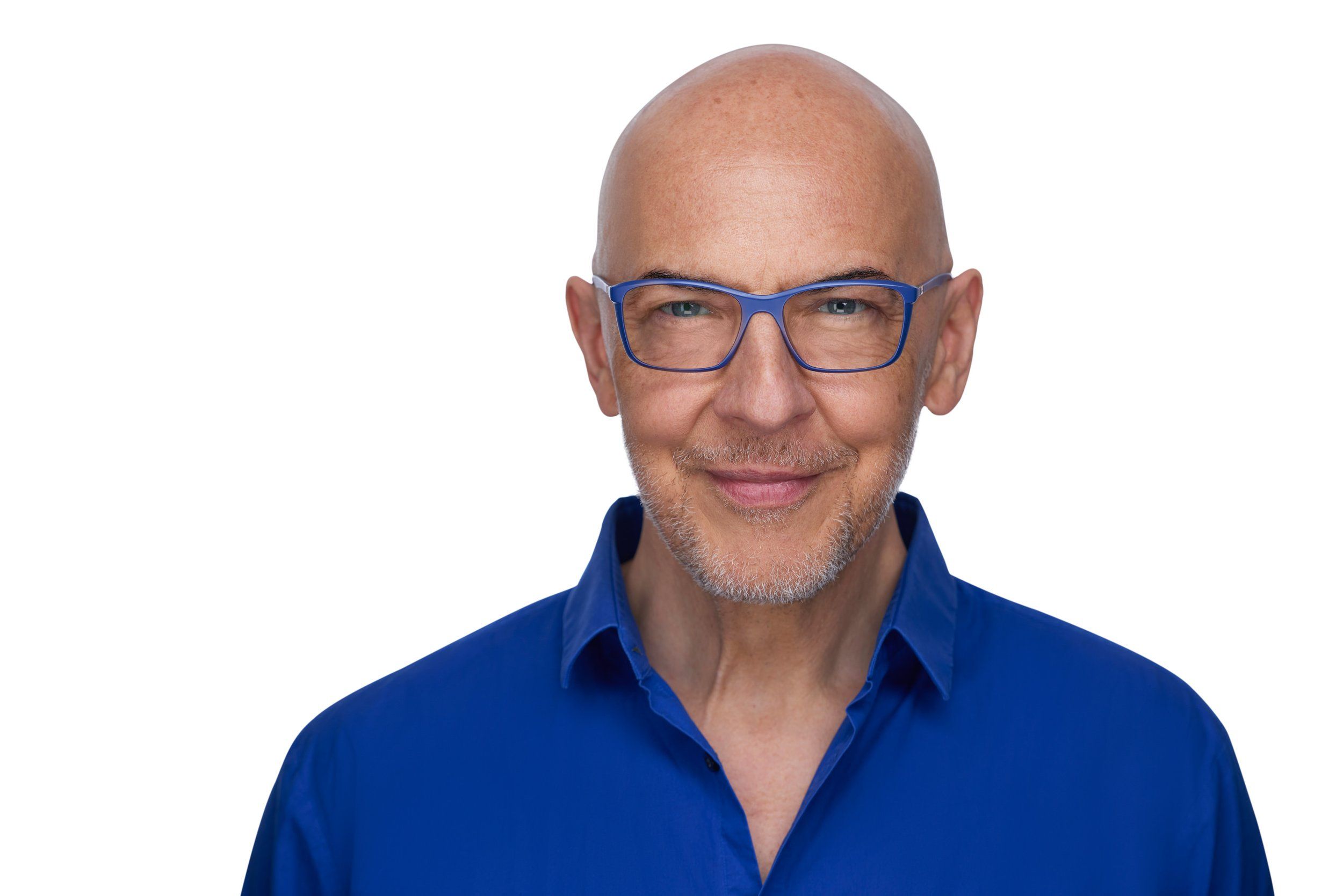 Headshot eines Mannes mit Glatze und blauer Brille im blauen Hemd vor weißem Hintergrund, fotografiert im Studio in Köln