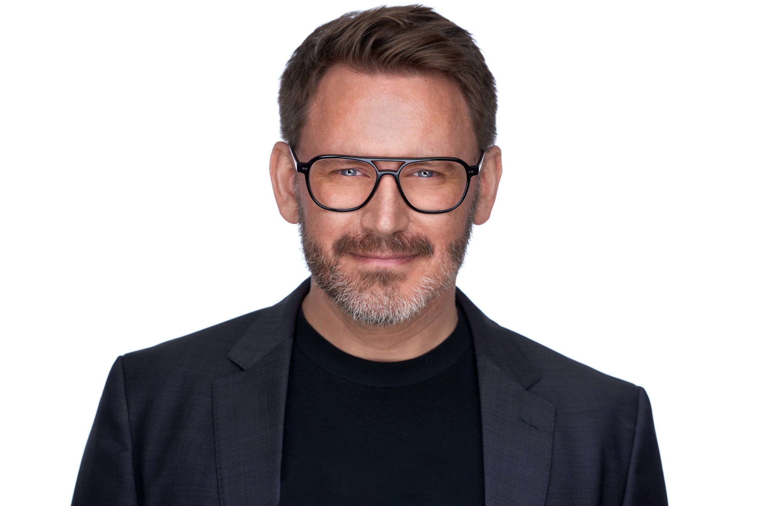 Headshot eines Mannes mit Brille und Bart im dunklen Sakko vor weißem Hintergrund, fotografiert im Studio in Köln