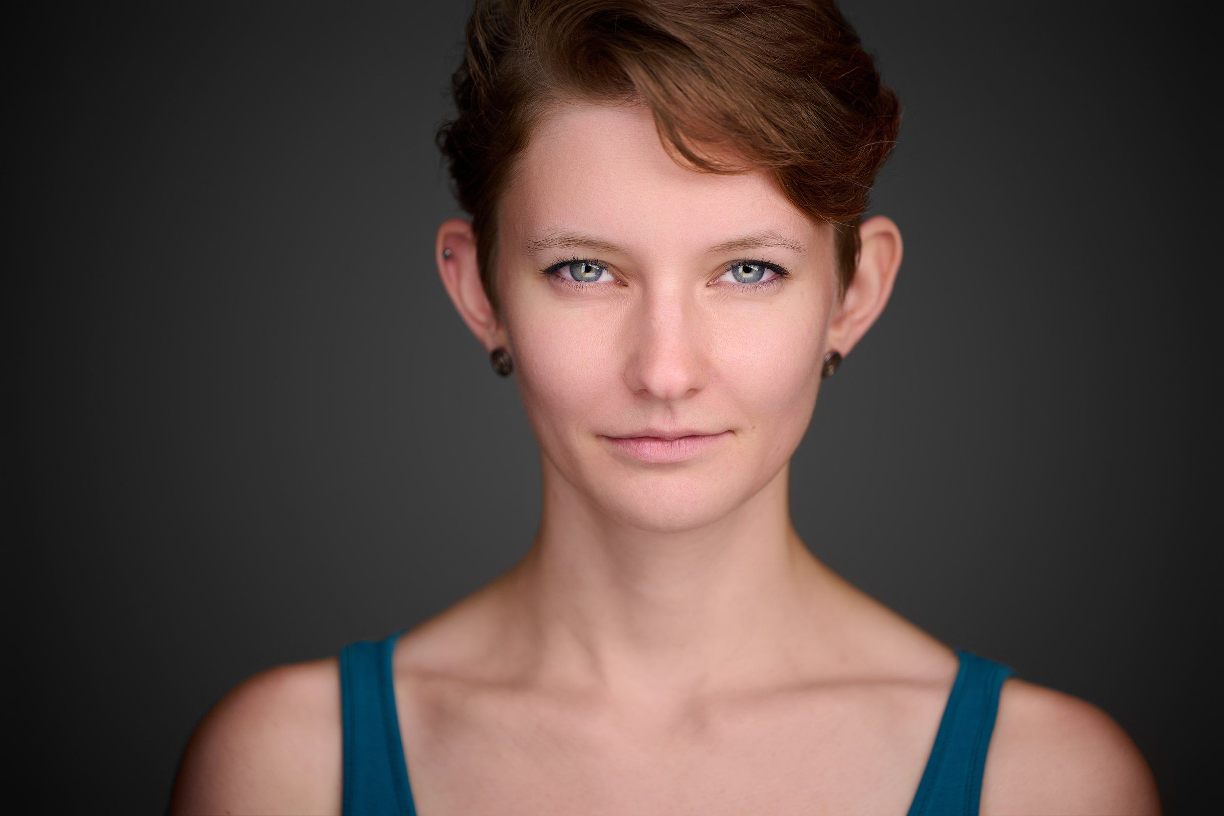 Schauspiel-Headshot einer jungen Frau mit kurzen rotbraunen Haaren vor dunklem Hintergrund, fotografiert im Studio in Köln